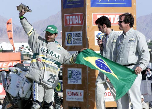 Jean levanta troféu e segura a bandeira brasileira com a ajuda de Hubert Auriol  organizador do Dakar. (foto: Ricardo Ribeiro / VipComm)