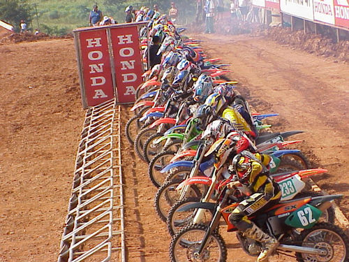 <i>Gate</i> de largada para as 250cc. (foto: Luciana de Oliveira)” /><br />
<i>Gate</i> de largada para as 250cc. (foto: Luciana de Oliveira)</div>
<p>O segundo dia de atividades em Jundiaí começou com o warm-up, espécie de treino de aquecimento e que também foi fundamental para que os pilotos sentissem como estava a pista depois das chuvas de sábado. O sol forte e o trabalho incansável de organizadores e Prefeitura resultou no chão mais seco, porém sem a tradicional poeira.</p>
<p><b>Open</b> – A categoria Open foi a primeira a entrar no circuito para decidir a etapa. A bateria começou pouco depois do meio-dia, no horário mais quente. No sábado, o melhor tempo havia sido de Cássio Roberto Garcia (Dimasa). E hoje o piloto confirmou o favoritismo com o tempo de 33min27. Em segundo ficou o veterano Ricardo Raspa (Honda – 33min45) que completou a prova mesmo com uma fratura na perna esquerda. Depois da bandeirada, ele foi socorrido pelos médicos e deverá ficar alguns meses fora das pistas.</p>
<p><b>60cc</b> – Na seqüência ocupou o <i>gate</i> de largada uma das categorias mais esperadas, 60 cilindradas. Nela estão os ´futuros campeões´ do motocross. São crianças e a maioria delas ingressou no esporte seguindo o rastro dos pais. Yoshinori Noda Filho (Moto China), de 12 anos, foi o primeiro colocado. Comecei em quinto e fui ultrapassando. Passei o primeiro colocado, depois ele recuperou e eu consegui ficar na frente dele no final, conta o pilotinho, que anda de Kawasaki. O tempo dele foi de 17min05. Em segundo ficou Anderson Cidade (Acerbis-Adventure), com Douglas Ricardo (ASW/Kawasaki) em terceiro.</p>
<p><b>80cc</b> – A bateria das 80cc parecia ter acertada a disputa pelo primeiro lugar entre Marcelo Ratinho Ferreira (Vaz/Yamaha/Kaerre) e Rafael Zenni (Honda), os dois mais rápidos no treino de ontem. Eles confirmavam a expectativa nas primeiras voltas, andando muito juntos. Tanto que acabaram se tocando, caindo e o guidão da moto de Zenni teria entrado na roda da moto de Ratinho. O segundo ainda se recuperou na prova em tempo de alcançar a 11ª colocação. Mas Zenni sofreu ainda com uma quebra da embreagem e terminou em 16º.</p>
<p>Com os dois fora da briga pelo pódio, quem fez a festa foi Renan Perini Buniy (Yamaha). Em segundo ficou Kurt Airton Rocha (Yamaha). Cristopher Castro (Honda) foi o terceiro e o piloto da casa, Matheus Storti (Oftalmo Clínica), o quarto.</p>
<p><b>125cc</b> – Roosevelt Assunção Jr (Honda) dominou a bateria das 125cc. A disputa mais acirrada foi pelo segundo e terceiro lugares. O atual campeão brasileiro da categoria, Ismael Pereira, foi sofrendo a pressão dos concorrentes. Primeiro, Pedro Lopes (Honda) lhe tomou o segundo lugar. Depois, Elton Becker (Cia Fox/Riffel) encostou, mas não conseguiu roubar a terceira posição do piloto de São Paulo.</p>
<p><b>250cc</b> – Para completar a festa da Honda, Antonio Jorge Balbi Jr largou na frente e não deu espaço a ninguém. Mas teve de abrir caminho durante toda a corrida. Eu ganhei uma boa vantagem, mas, como a pista era curta, tive muitos retardatários pela frente. Não teve uma volta sem que eu não tivesse que ultrapassar alguém, comentou, após a festa no pódio completado por Milton Chumbinho Becker (Yamaha), em segundo; Massoud Nassar Neto (Honda), em terceiro; Rodrigo Dias Siqueira (Suzuki) em quarto e Paulo Stédile (Tork/Virilon/Yamaha), em quinto.</p>
<p><strong><em>Este texto foi escrito por: Luciana de Oliveira</em></strong></p>
<div class=